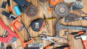 Várias ferramentas manuais e elétricas espalhadas sobre uma mesa de madeira, incluindo martelo, alicate, fita métrica, chave Allen, serra e discos de esmeril.